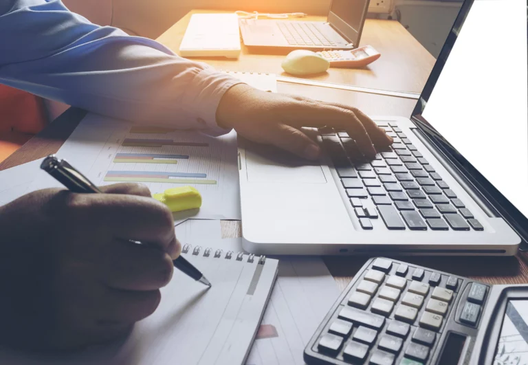 a office worker and copy writer writing blog content using a laptop with right hand holding a pen to take notes