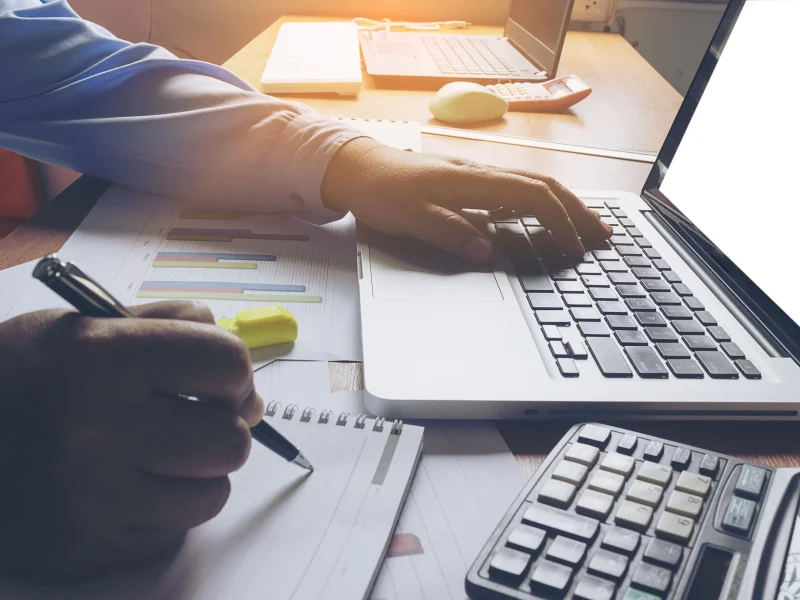 a office worker and copy writer writing blog content using a laptop with right hand holding a pen to take notes